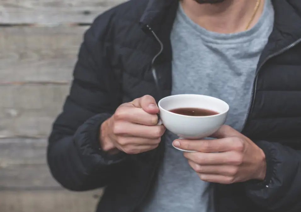  رجل يحمل كوبًا من الشاي، يوحي بفوائد الحلبة الطبيعية للانتصاب والطاقة والخصوبة لدى الرجال.