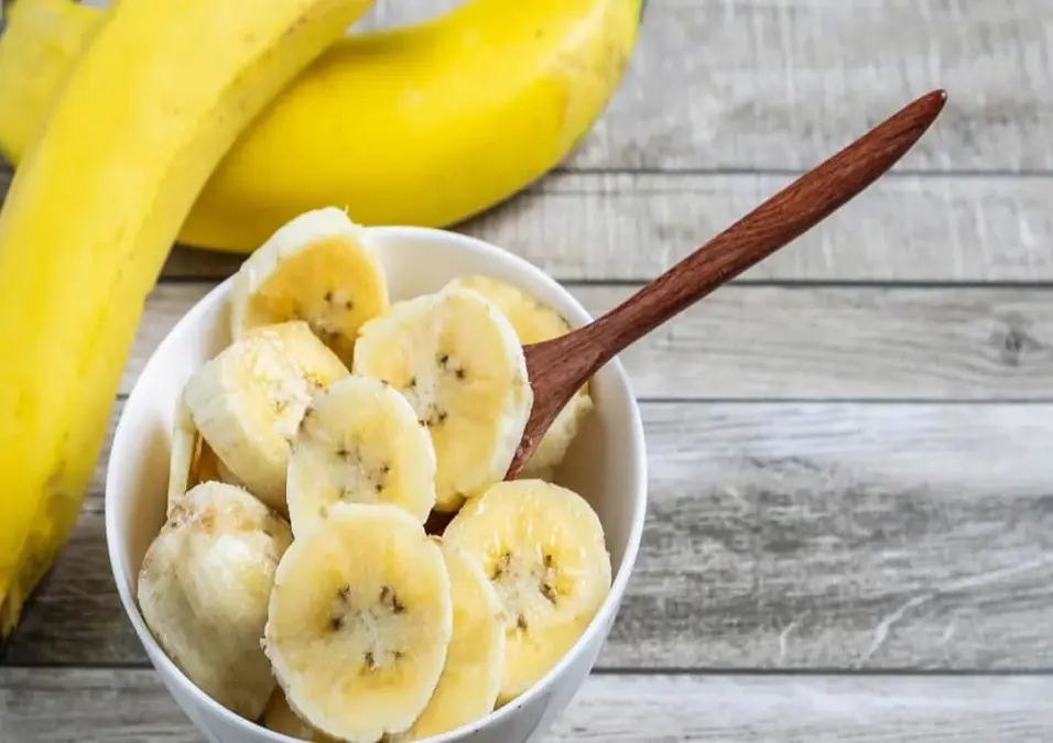 وعاء من الموز المقطع مع ملعقة خشبية، يوحي بفوائد الفاكهة قبل النوم.