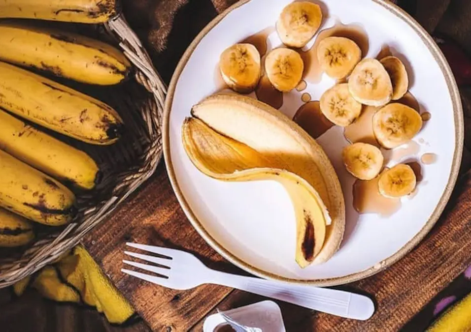 طبق من الموز المقشر والمقطع بجوار سلة من الموز الكامل، يوحي بفوائد هذه الفاكهة لصحة الجسم والقلب.