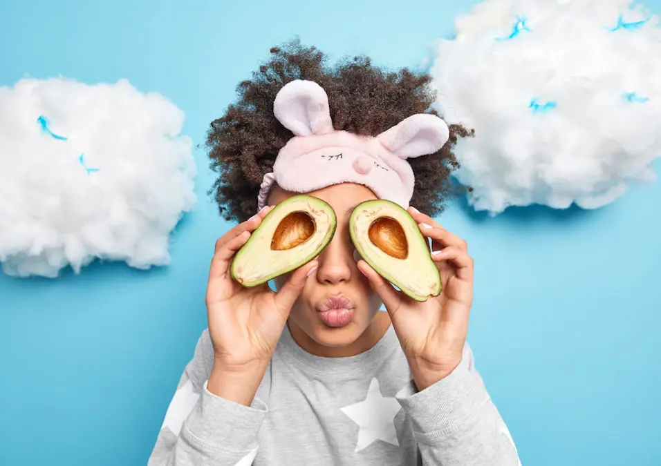  شخص يحمل نصفي أفوكادو فوق عينيه، يقوم بتعبير وجه مرح، يوحي بفوائد الأفوكادو للأطفال.