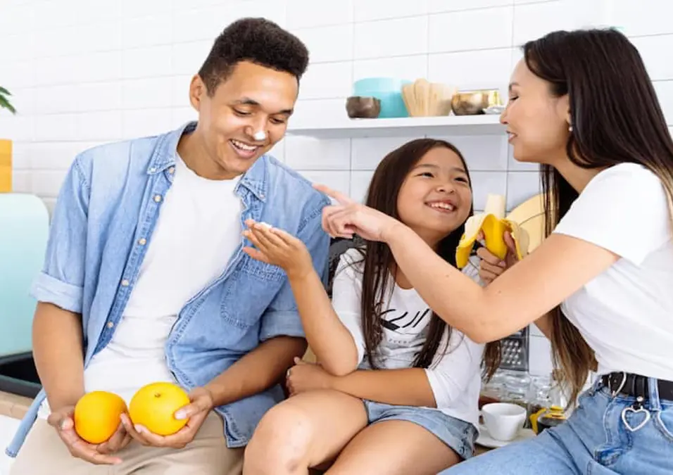 عائلة في المطبخ تتقاسم الموز وتمرح بالطعام، توحي بفوائد الموز للأطفال.