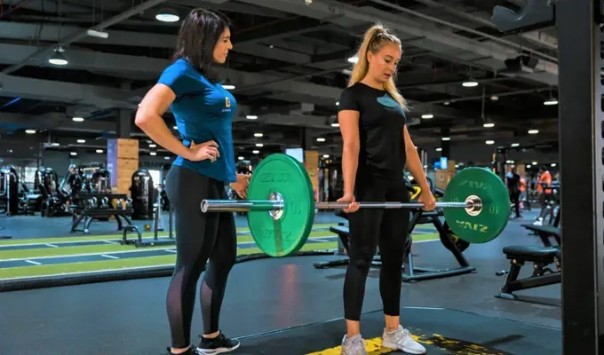 A coach assisting an individual with a barbell lift in a gym environment
