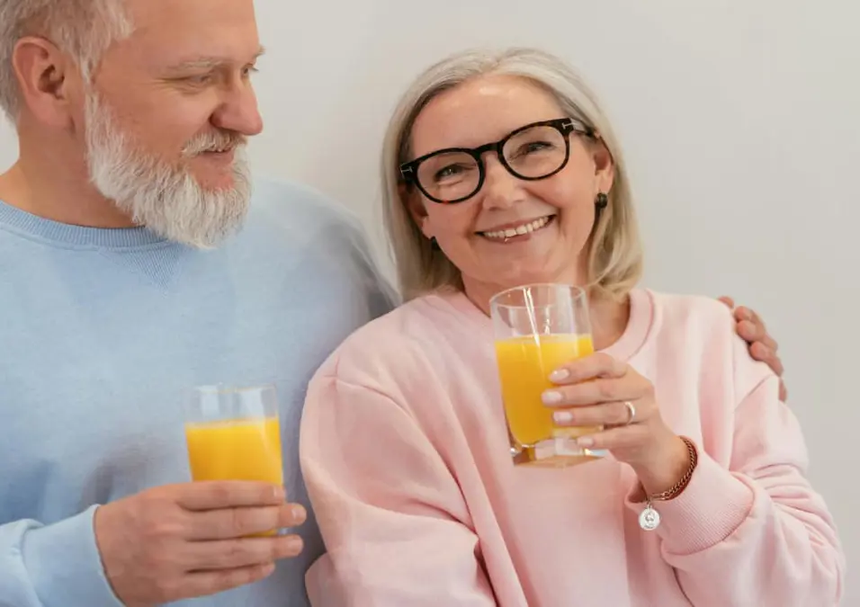 زوجان مسنان مبتسمان يحملان أكواب عصير برتقال، يمثلان تجارب حقيقية لحالات شفيت من الضغط المرتفع.