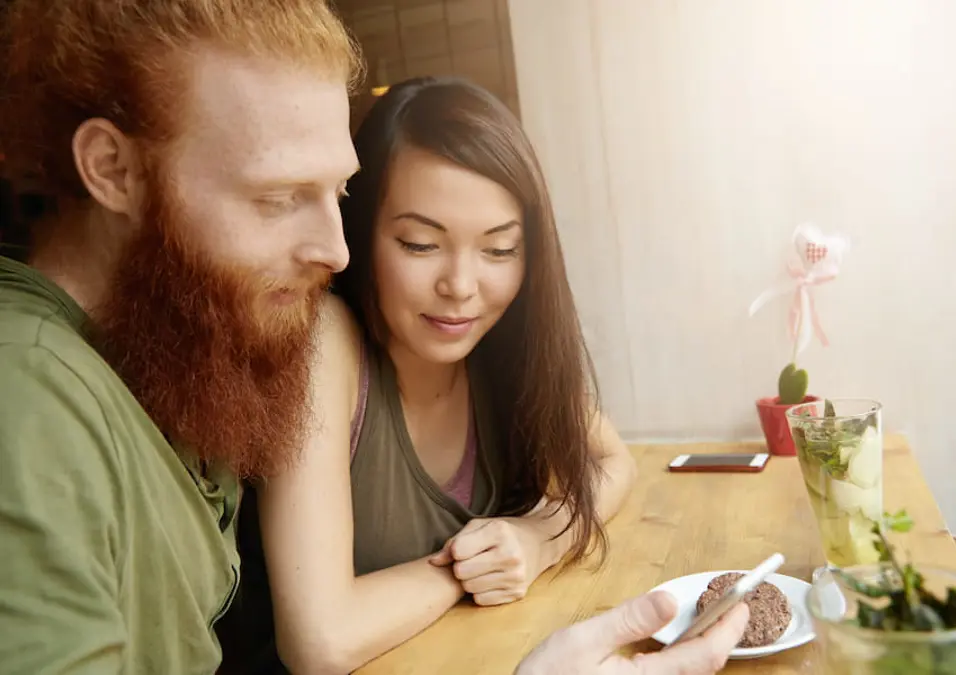 رجل بلحية حمراء وامرأة يجلسان معاً في مقهى وينظران إلى هاتف، يوحي بالدور المحتمل للشمر لخصوبة وصحة الرجال الجنسية.