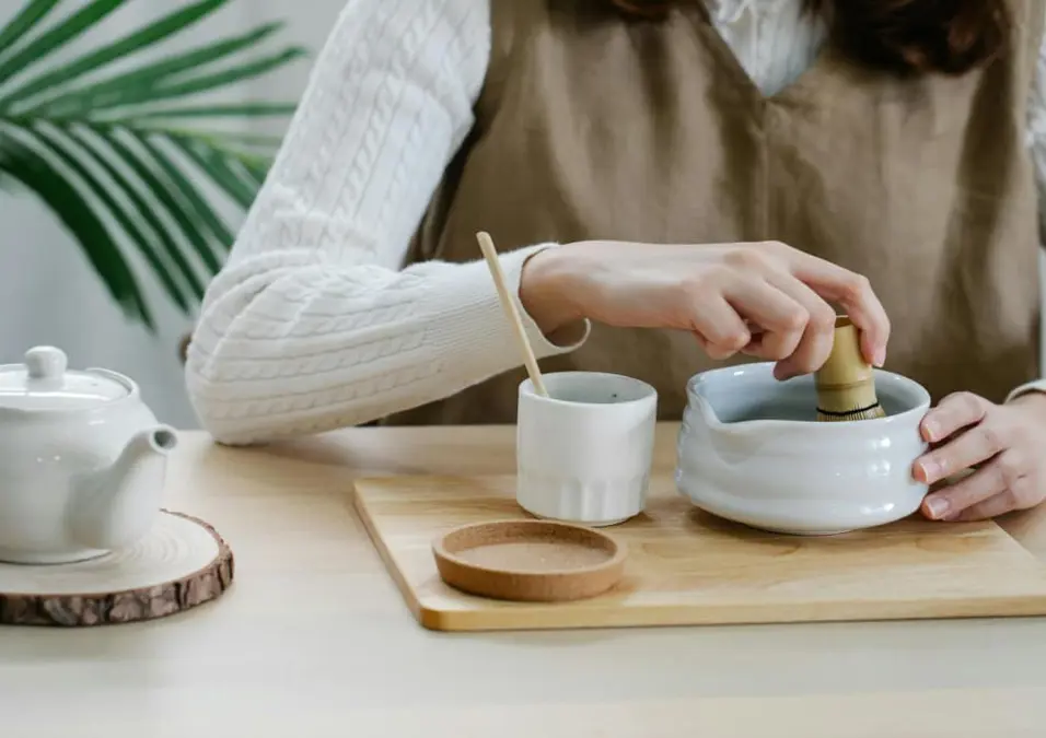 امرأة تحضر شاي الماتشا باستخدام المضرب، توحي بفوائد الماتشا للنساء.