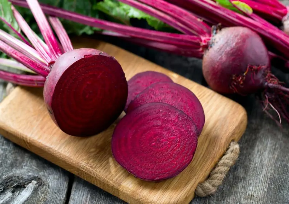 شمندر مقطع على لوح تقطيع خشبي مع حبات كاملة وأوراق خضراء في الخلفية، يوحي بقيمته الغذائية وطرق استخدامه وأضراره المحتملة.