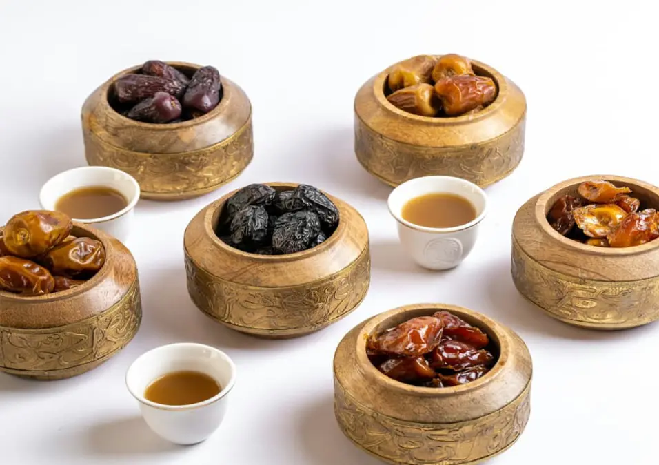 أنواع مختلفة من التمر في أوعية خشبية مزخرفة مع أكواب قهوة صغيرة، تدعو لمعرفة دقيقة لعدد السعرات الحرارية في التمر.