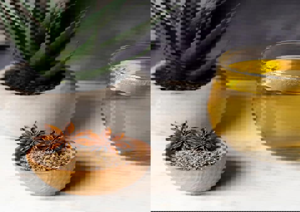 وعاء من بذور اليانسون واليانسون النجمي بجانب كوب من شاي اليانسون، يوحي بفوائد اليانسون كعلاج طبيعي للقولون والمعدة.