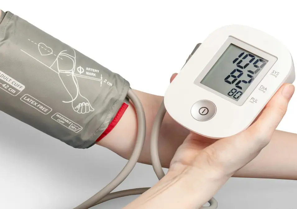 ذراع شخص مع جهاز قياس ضغط الدم يعرض قراءة، يناقش متى يبدأ الضغط المرتفع، أعراضه، مضاعفاته، وعلاجه بالتفصيل.