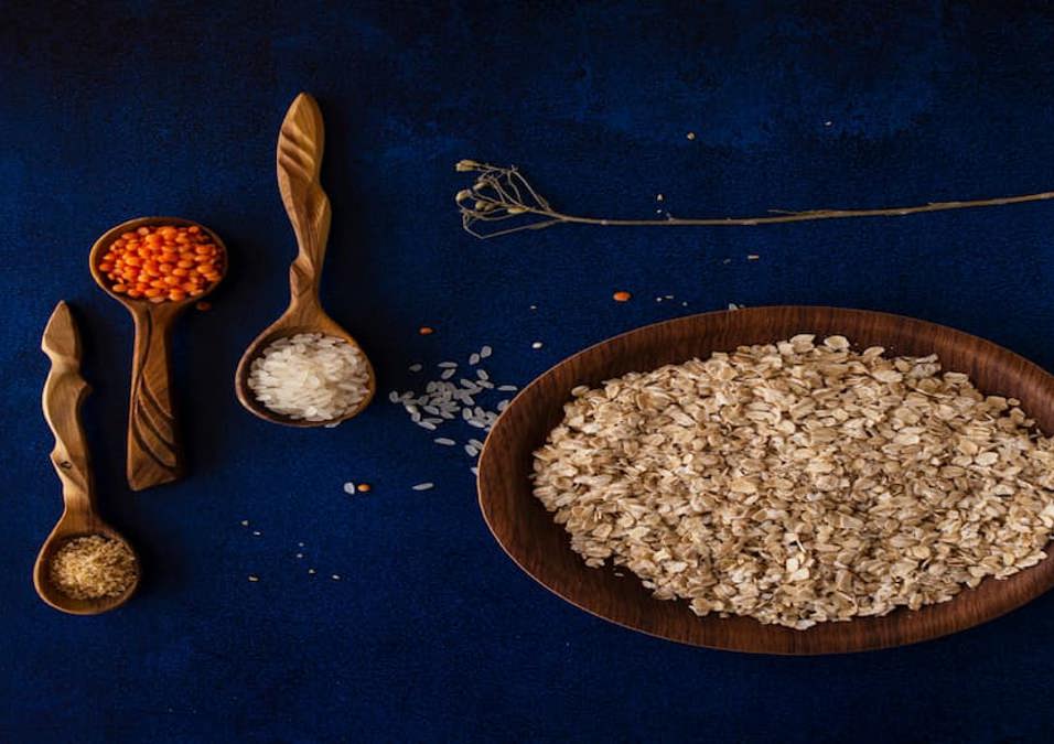 وعاء من الشوفان مع ملاعق خشبية تحمل حبوب وبهارات، يستكشف عدد السعرات الحرارية في الشوفان.