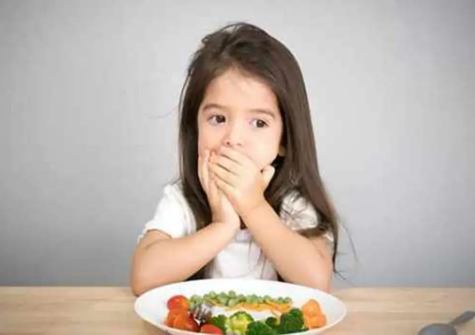  فتاة صغيرة تغطي فمها وهي تنظر إلى طبق من الخضروات، تشير إلى أعراض نقص الحديد لدى الأطفال.