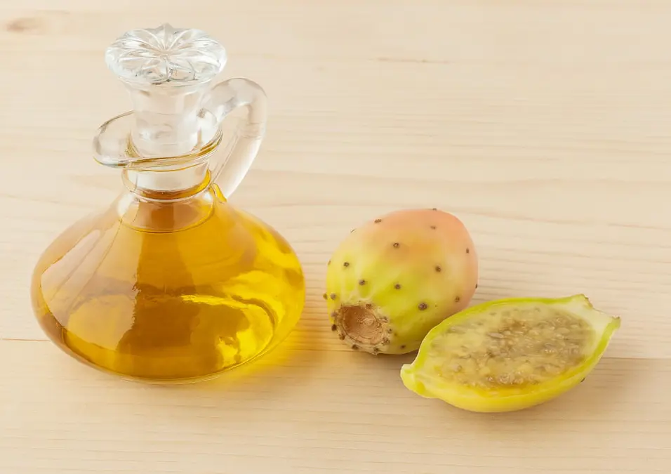 زجاجة صغيرة من زيت التين الشوكي بجانب ثمرة تين شوكي كاملة ومقطعة، توحي بالنتائج المذهلة والتجارب الحقيقية لفوائد زيت التين الشوكي للوجه.