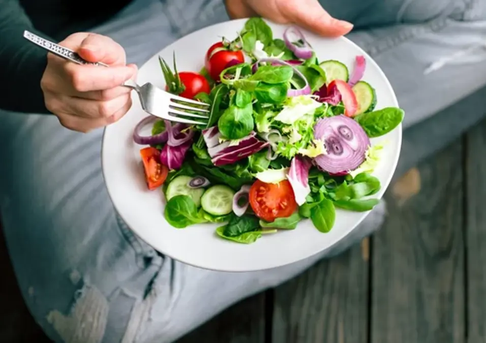 A Person Sitting On The Floor Eating A Healthy Salad