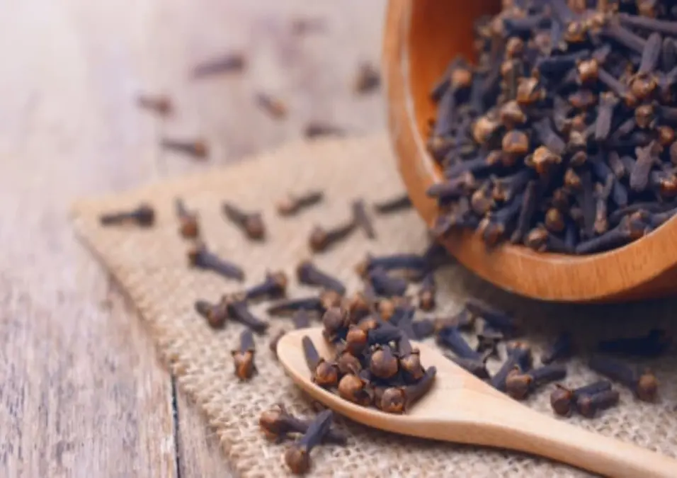 ملعقة خشبية صغيرة ووعاء خشبي يفيضان بالقرنفل على سطح من الخيش، مما يوحي بفوائد القرنفل للجنس، والحقيقة الكاملة والاستخدام الصحيح.