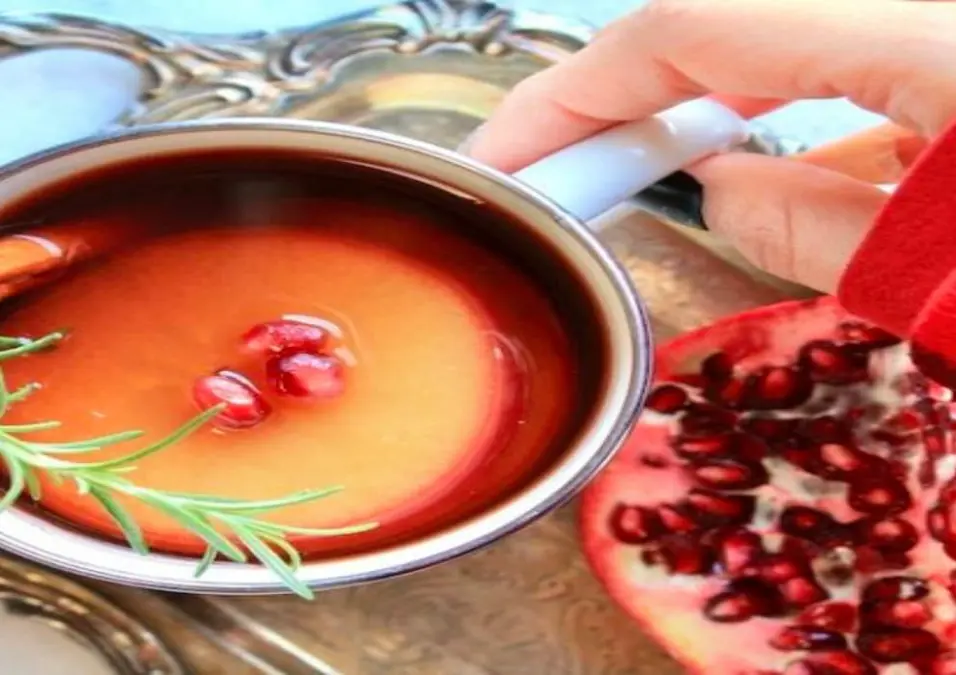 كوب من شاي الرمان الساخن مزين بعود قرفة وإكليل الجبل، يوحي بفوائده قبل النوم.