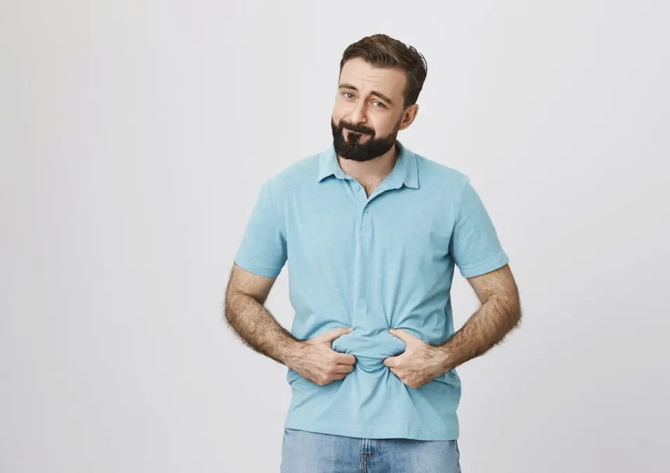 رجل يمسك معدته يشير الى الدهون الحشوية.