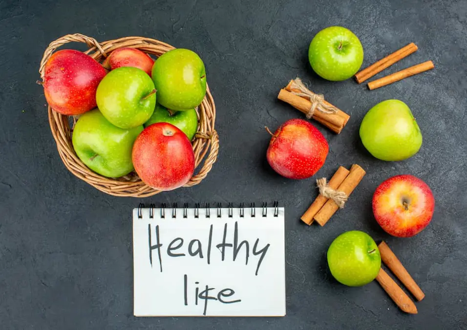 سلة من التفاح الأحمر والأخضر مع أعواد القرفة ودفتر مكتوب عليه 