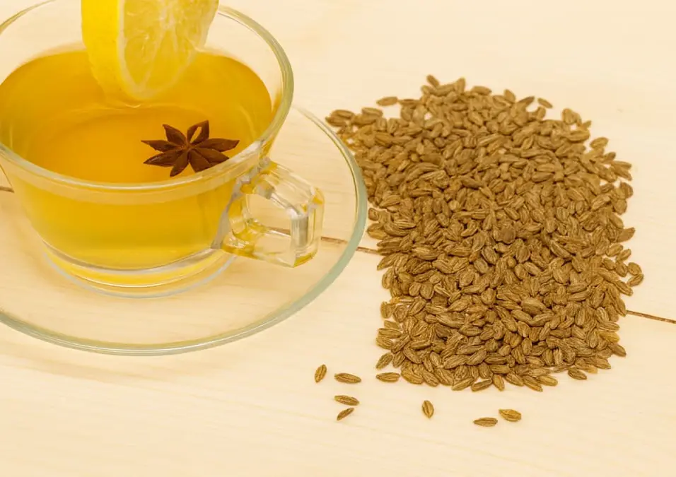 كوب من شاي اليانسون مع شريحة ليمون ويانسون نجمي، مع كومة من بذور اليانسون على طاولة خشبية، يوحي بفوائد اليانسون للرجال.