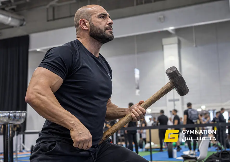 A strong, muscular figure dominates the scene, gripping a hammer. Bold letters form a vibrant backdrop. The lighting