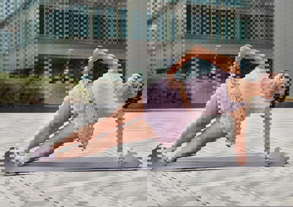 امرأة تؤدي تمرين البلانك الجانبي في الهواء الطلق، توضح حركات لنحت الخصر وشد البطن.