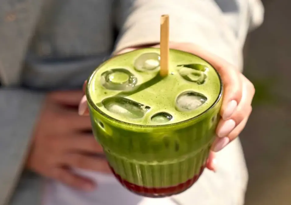 شخص يحمل كوبًا من الماتشا المثلج، يوحي بتساؤل حول ما إذا كانت أضرار الماتشا حقيقة أم مبالغة.