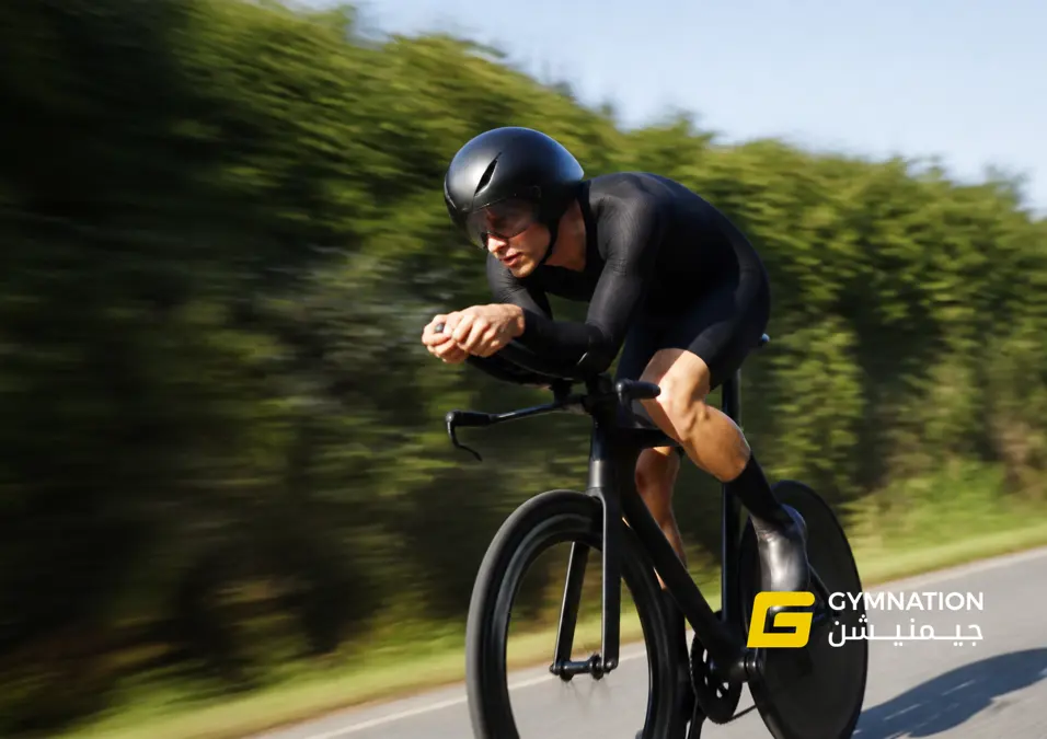 A cyclist speeds along a path, leaning forward in an aerodynamic posture. Surrounding greenery blurs in the background