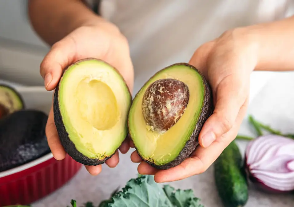 يد تحمل نصفي ثمرة أفوكادو طازجة، توحي بفوائدها العديدة للصحة والجمال.