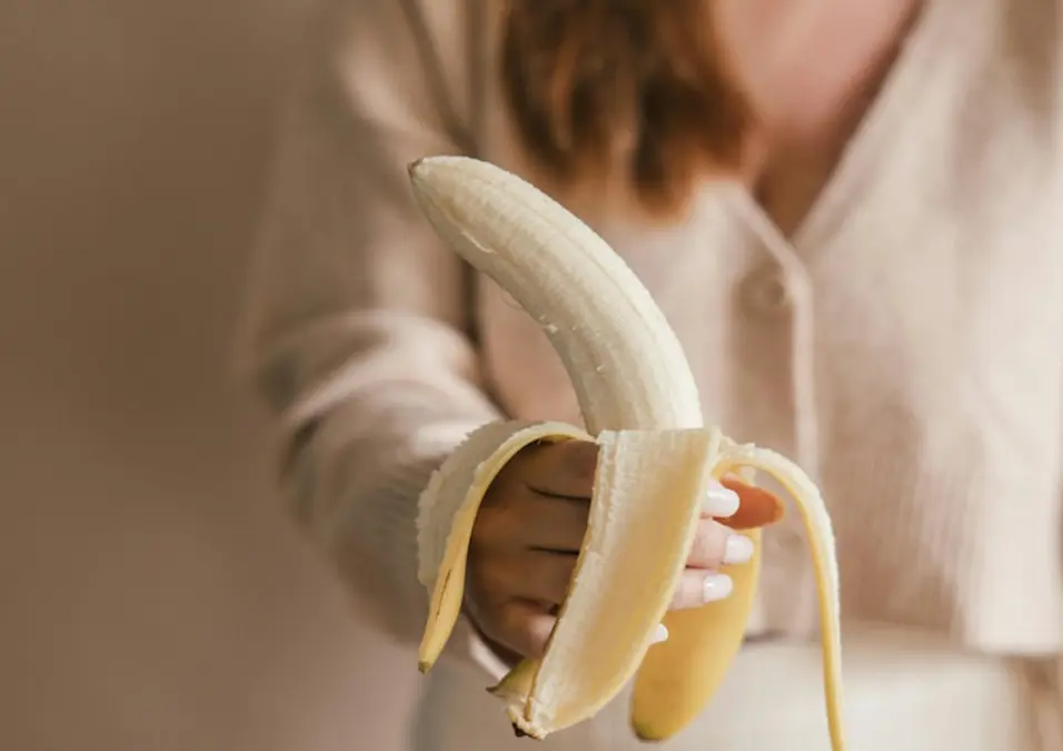 امرأة تحمل موزة مقشرة جزئياً، توحي بفوائد الموز للنساء.
